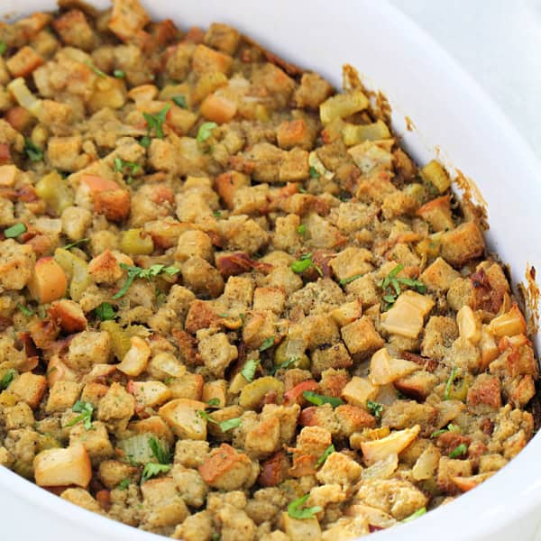 A casserole dish filled with bread stuffing, featuring cube-shaped bread pieces and green herbs.