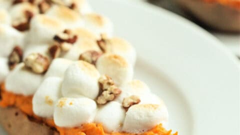 Twice-baked sweet potato topped with marshmallows and chopped nuts on a white plate.