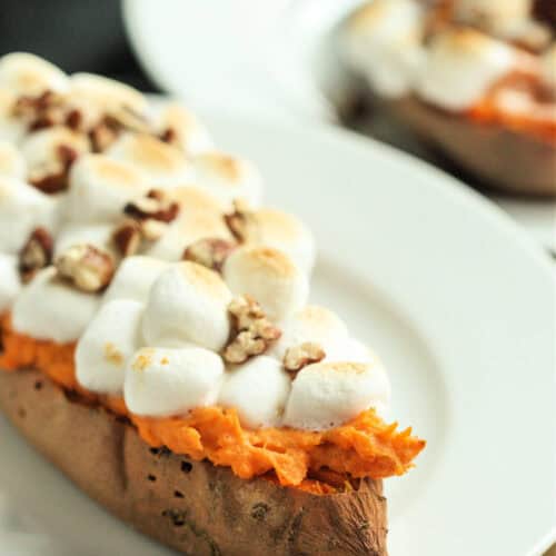 Twice-baked sweet potato topped with marshmallows and chopped nuts on a white plate.