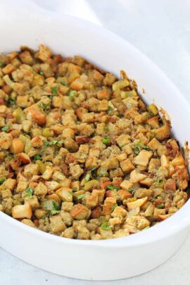 A white casserole dish filled with seasoned croutons and herbs, baked to a golden brown.