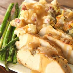 Plate with sliced turkey breast topped with gravy, green asparagus, mashed potatoes, and stuffing.