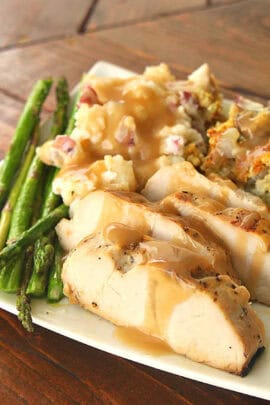 Plate with sliced turkey breast topped with gravy, green asparagus, mashed potatoes, and stuffing.