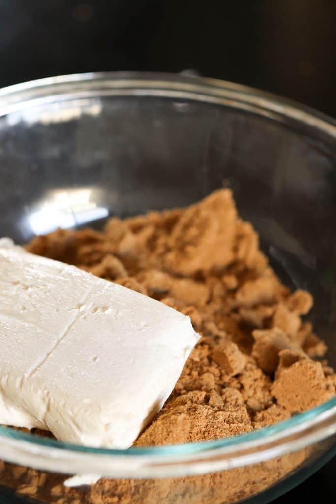 A brick of cream cheese and gingersnap crumbs in a glass mixing bowl.