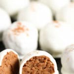 Close-up of white chocolate truffles, with the one in the foreground showing a bite taken out, revealing a peanut butter filling.