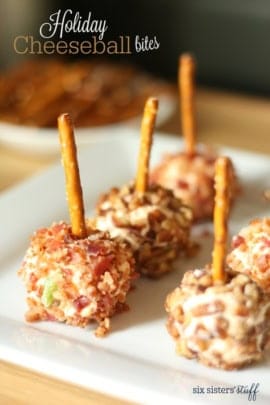 Small cheese balls coated with chopped nuts and bacon, each with a pretzel stick in the center, arranged on a white plate.