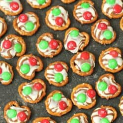 Pretzels topped with melted chocolate and red and green candies arranged on a dark surface.