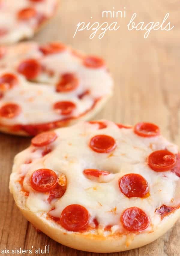 Four mini Texas toast pizzas topped with melted cheese and pepperoni slices on a wooden surface; a small pile of pepperoni slices is seen in the background.