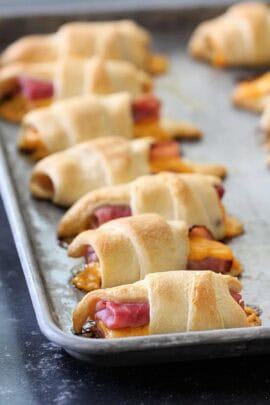 Golden brown crescent rolls filled with ham and melted cheese are lined up on a baking sheet.