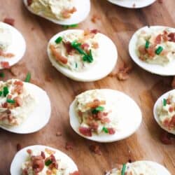 Deviled eggs topped with bacon and chives on a wooden board.