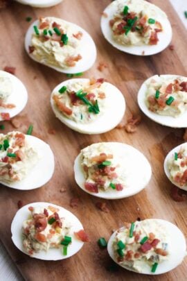 Deviled eggs topped with bacon and chives on a wooden board.