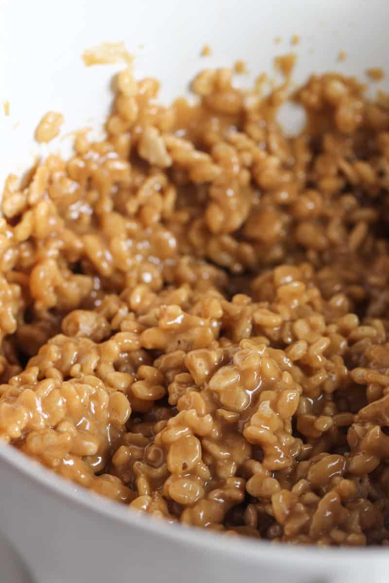 Rice Krispies with peanut butter mixture stirred together in a mixing bowl.