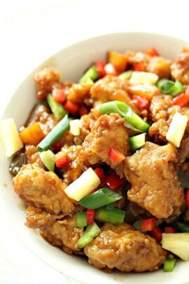 Close-up of a plate of sweet and sour chicken with colorful bell peppers, pineapple chunks, and green onions.