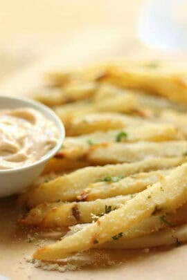 Close-up of seasoned crispy fries served with a small bowl of dipping sauce on the side.