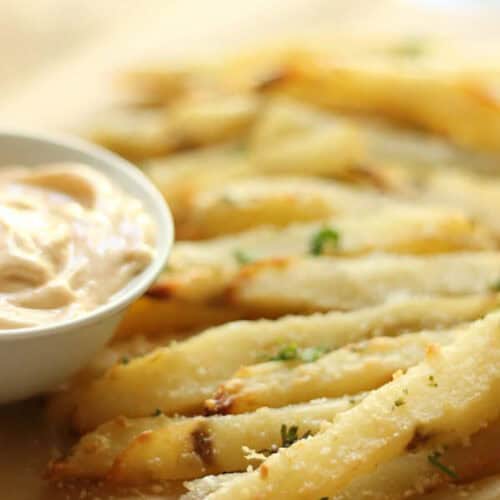 Close-up of seasoned crispy fries served with a small bowl of dipping sauce on the side.