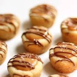 A close-up of nine small caramel-filled pastries drizzled with chocolate, arranged in rows on a white surface.