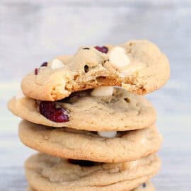 A stack of four cookies with white chocolate chips and dried cranberries, with a bite taken out of the top cookie.