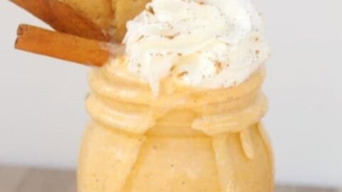 A mason jar filled with a creamy pumpkin pie milkshake, topped with whipped cream, two cinnamon sticks, and two graham crackers.