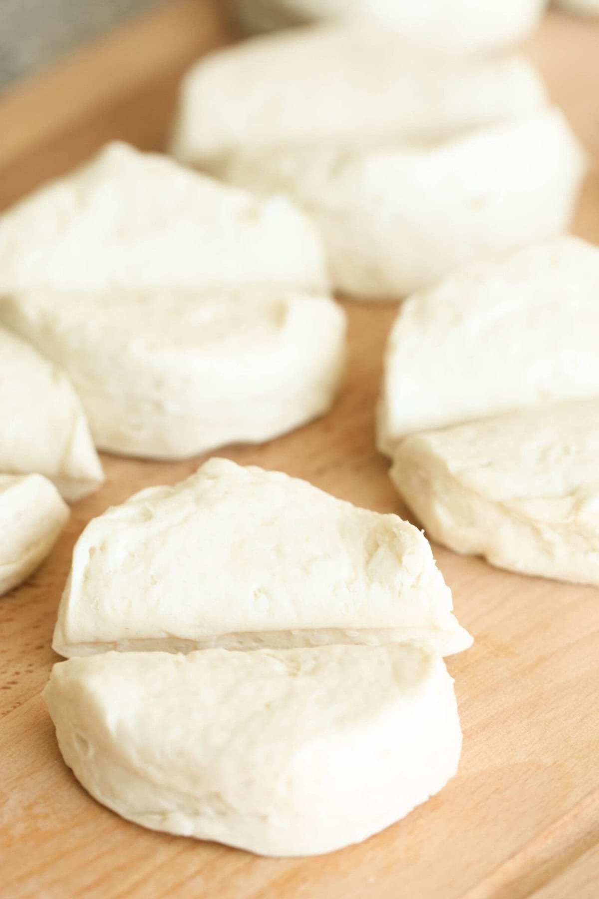 Close-up of several pieces of biscuit dough on a wooden surface, ready for baking.