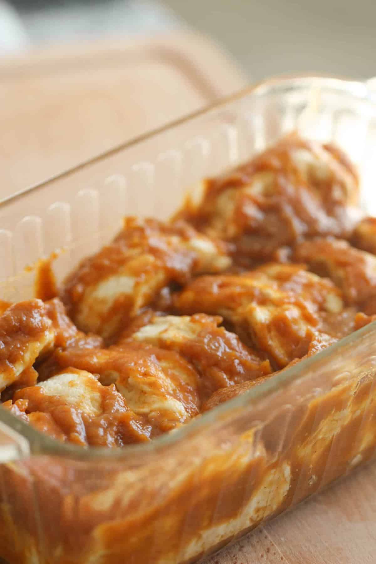 A glass baking dish filled with chicken pieces covered in a thick, reddish-brown sauce.