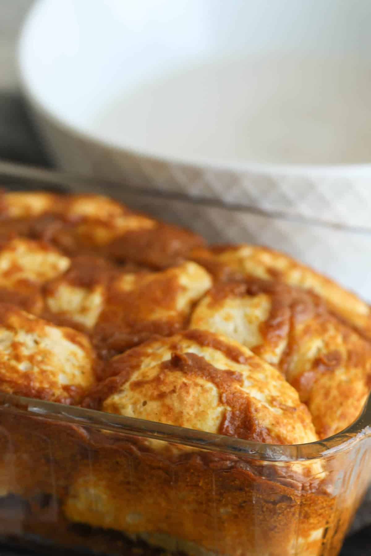 A rectangular glass baking dish filled with browned, baked bread rolls sits in front of a white bowl.