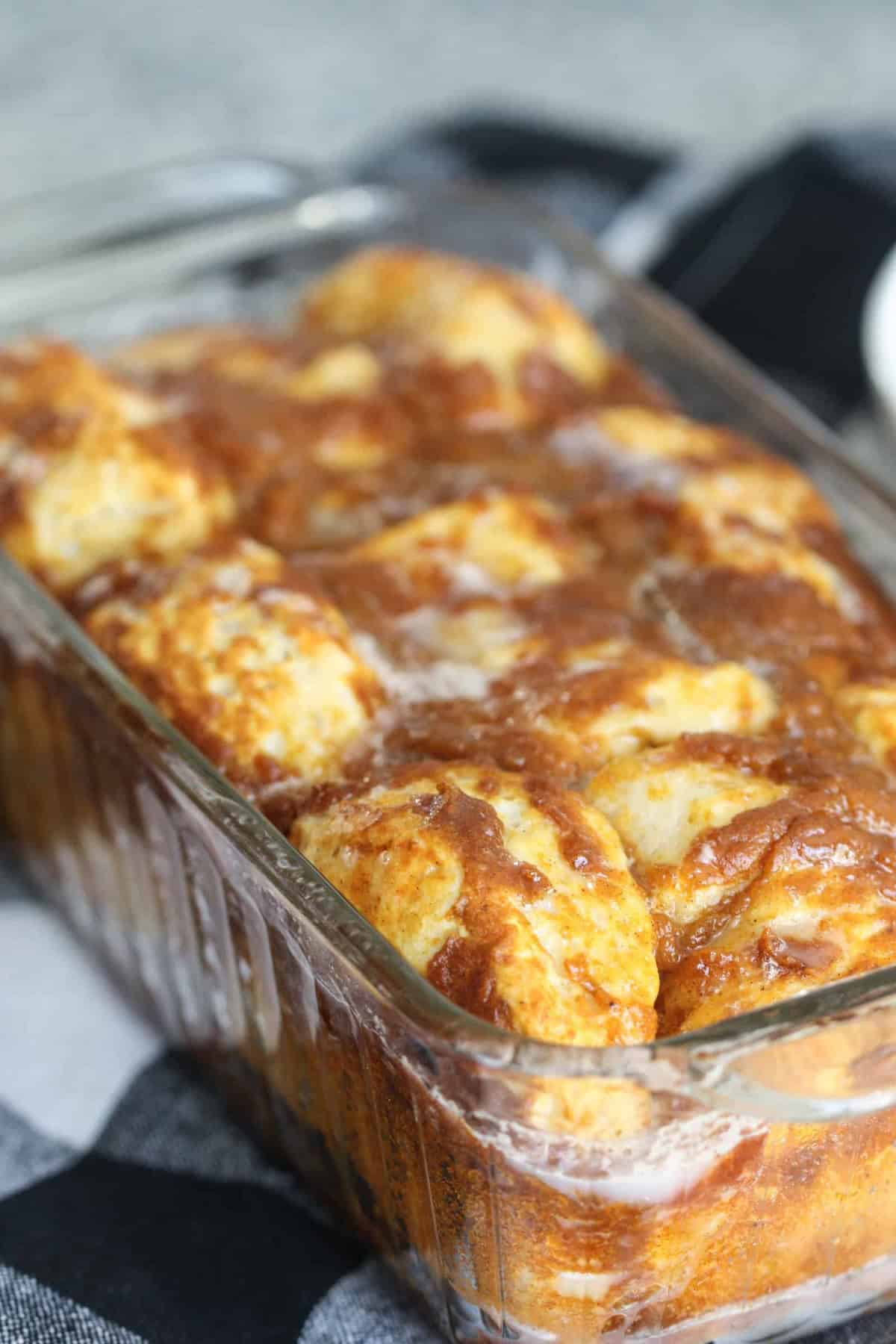 A glass baking dish contains freshly baked, golden brown pull-apart bread with visible cinnamon and sugar glaze.