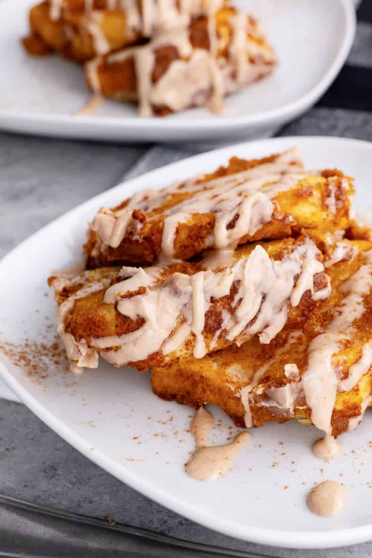 Three pieces of pumpkin pull apart bread drizzled with icing are served on a white plate, with another similar plate in the background.