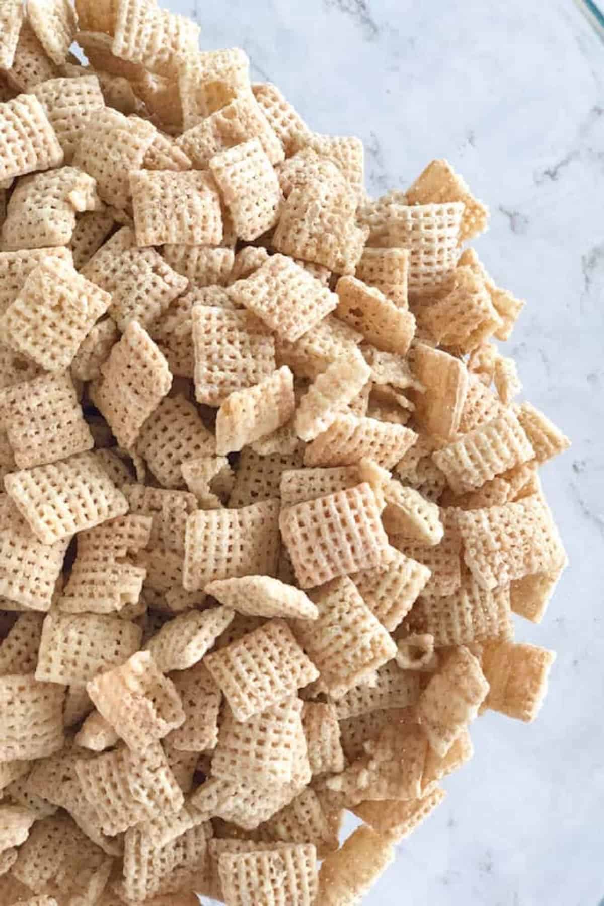 Close-up of a pile of square-shaped breakfast cereal pieces with a grid pattern, scattered over a marble surface.