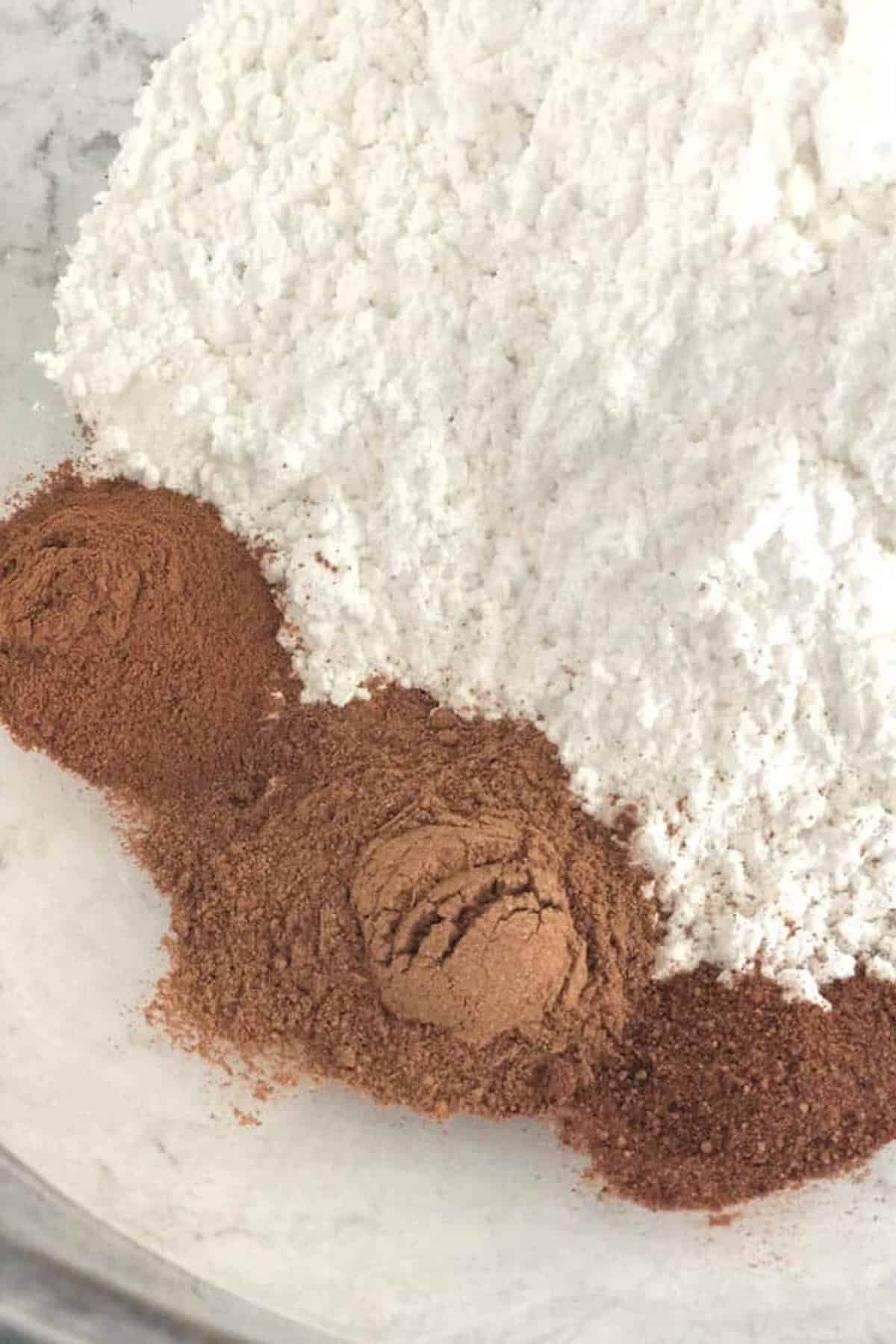 A bowl containing a mound of white flour and three distinct small piles of cocoa powder.