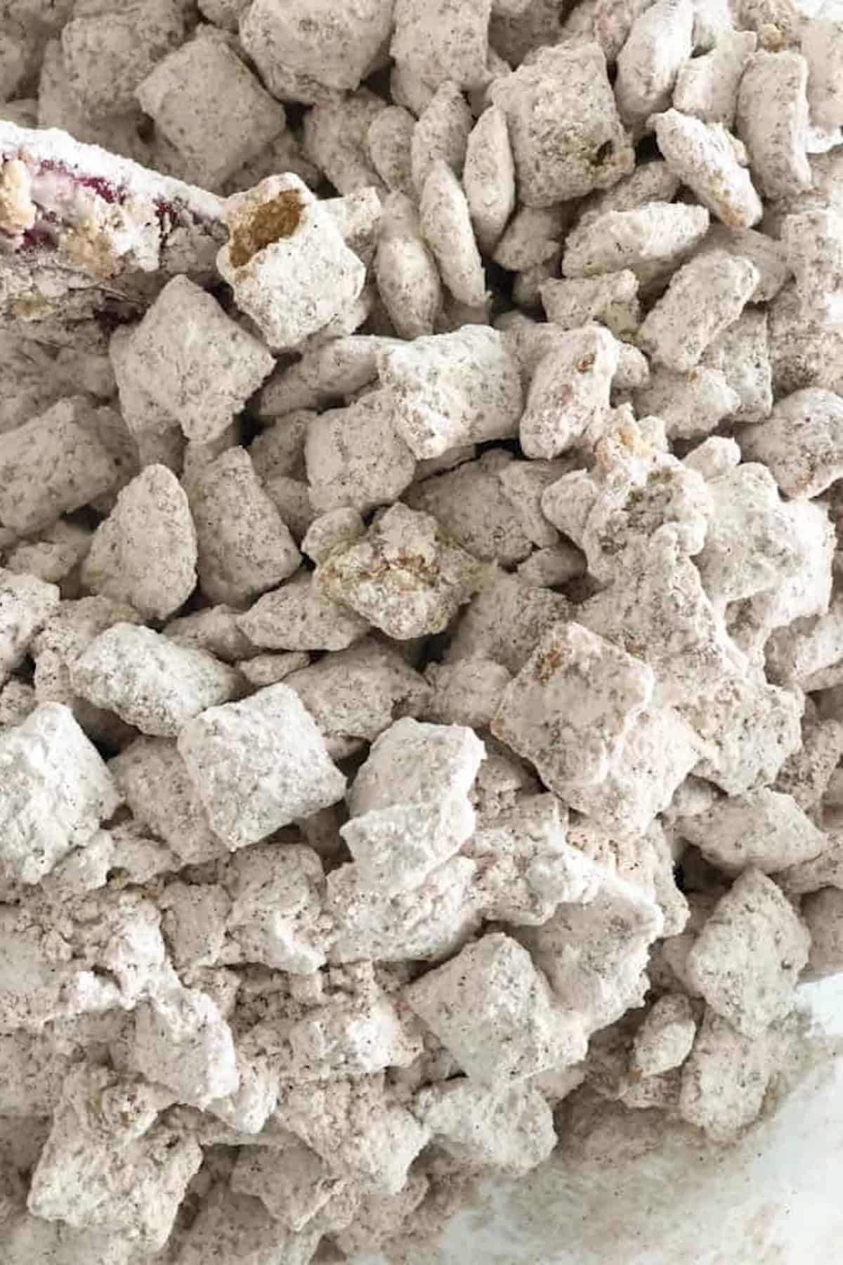 Close-up of a pile of white, powdered sugar-coated Chex cereal pieces, often referred to as "puppy chow" or "muddy buddies.