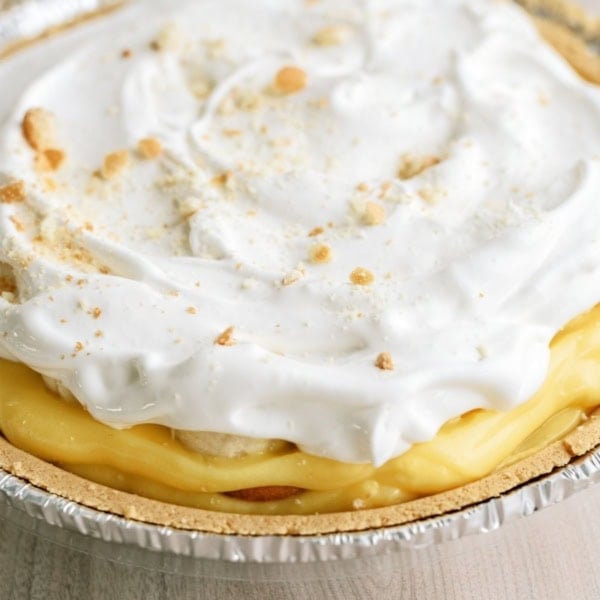 A close-up of a cream pie with a golden crust and a topping of whipped cream and sprinkled crumbs.