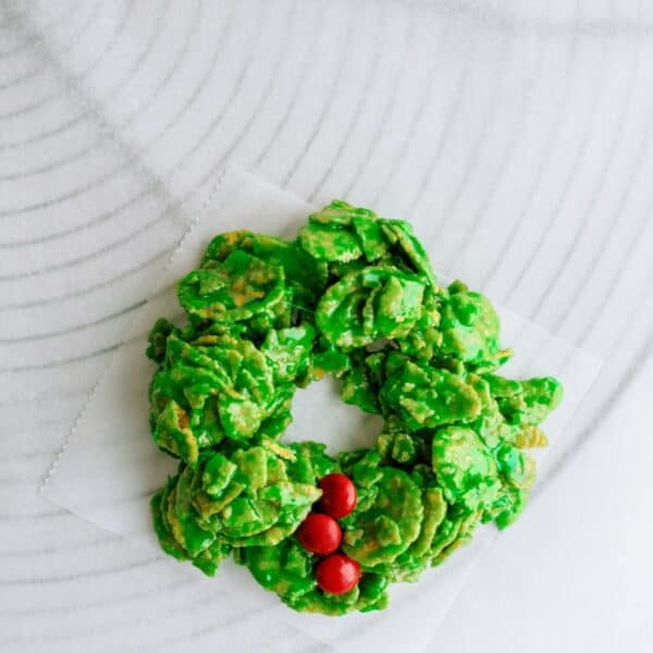 A festive green cornflake wreath with red candy decorations arranged on a white surface.