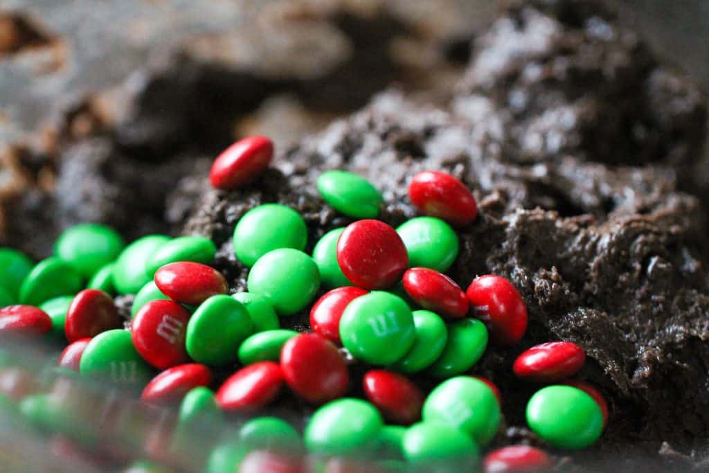 Adding M&M's into cake mix mixture in glass mixing bowl.