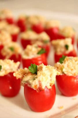 Stuffed cherry tomatoes filled with creamy mixture and topped with breadcrumbs, garnished with parsley, arranged on a plate.