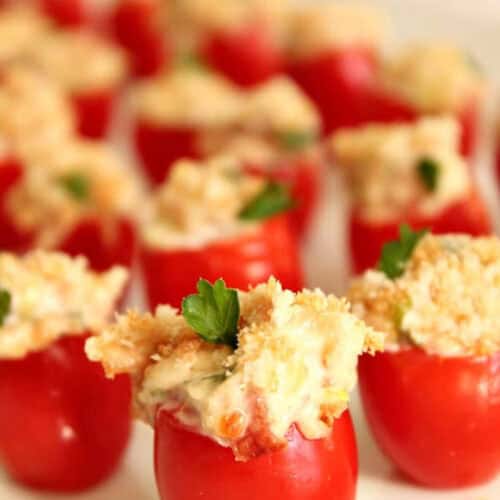 Stuffed cherry tomatoes filled with creamy mixture and topped with breadcrumbs, garnished with parsley, arranged on a plate.