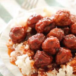 A plate of white rice topped with glazed meatballs, placed on a green and white striped cloth with a fork in the background.