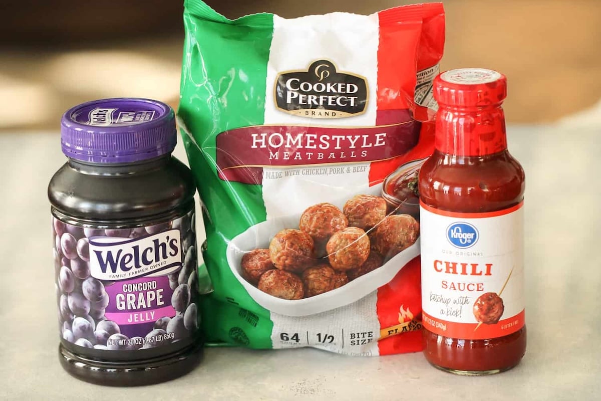 A jar of Welch's grape jelly, a bag of Homestyle meatballs, and a bottle of Kroger chili sauce are placed side by side on a countertop.