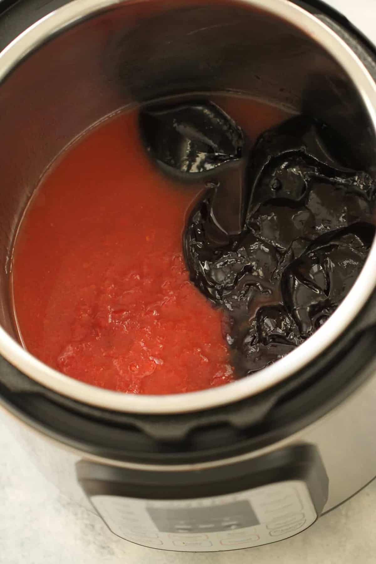 An electric pressure cooker containing red sauce and rehydrating dried chile peppers.