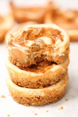 Stack of three mini cheesecakes with a swirl of caramel on top. A bite is taken out of the top cheesecake, revealing a creamy interior and crumbly crust.