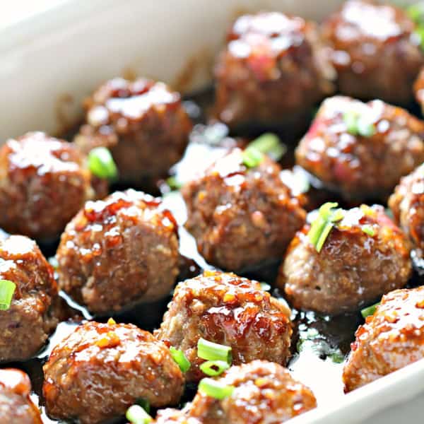 A baking dish filled with cooked glazed meatballs, garnished with chopped green onions.