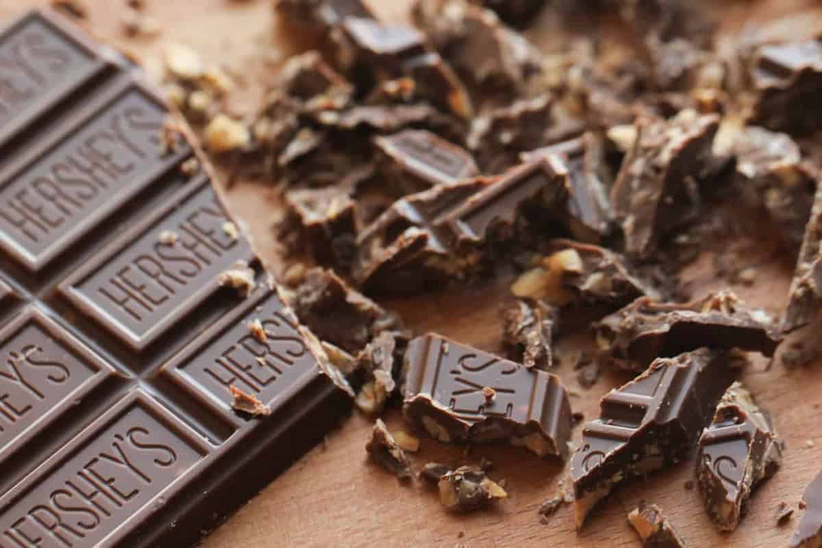 A Hershey's chocolate bar partially broken, with scattered pieces on a wooden surface.