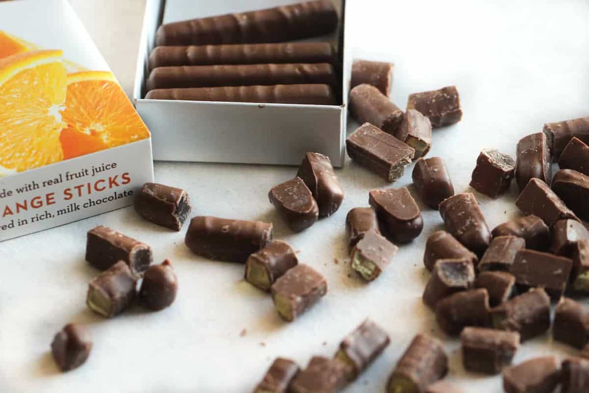 Box of chocolate-covered orange sticks with many pieces scattered around on a white surface.