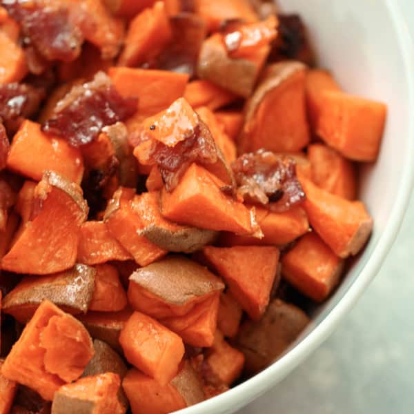 A bowl containing diced cooked sweet potatoes and pieces of dark-colored dates.