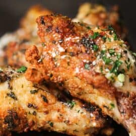 Close-up of garlic parmesan chicken wings cooked in an air fryer, garnished with herbs and grated parmesan.