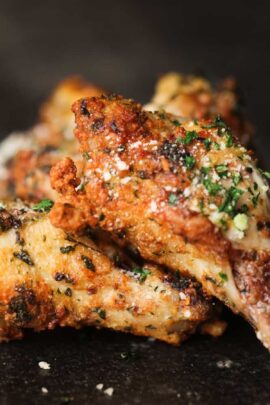 Close-up of garlic parmesan chicken wings cooked in an air fryer, garnished with herbs and grated parmesan.