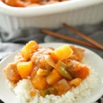 A plate with rice topped with a serving of Easy Baked Sweet and Sour Pork. With more Easy Baked Sweet and Sour Pork in the background.