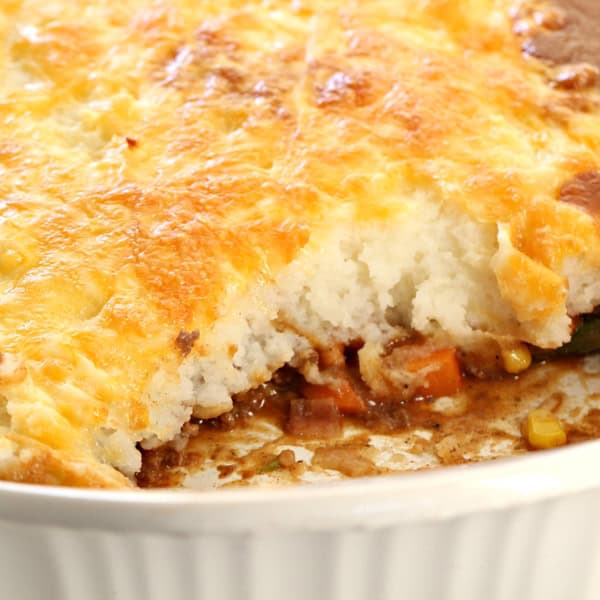A close-up of a partially eaten shepherd's pie in a white ceramic baking dish, showing layers of mashed potatoes, meat, and mixed vegetables.
