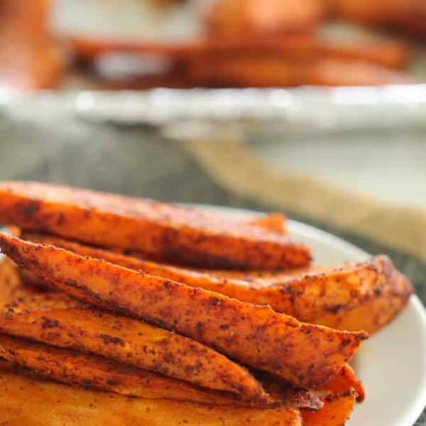 A plate of seasoned sweet potato fries with a small bowl of red dipping sauce in the foreground.