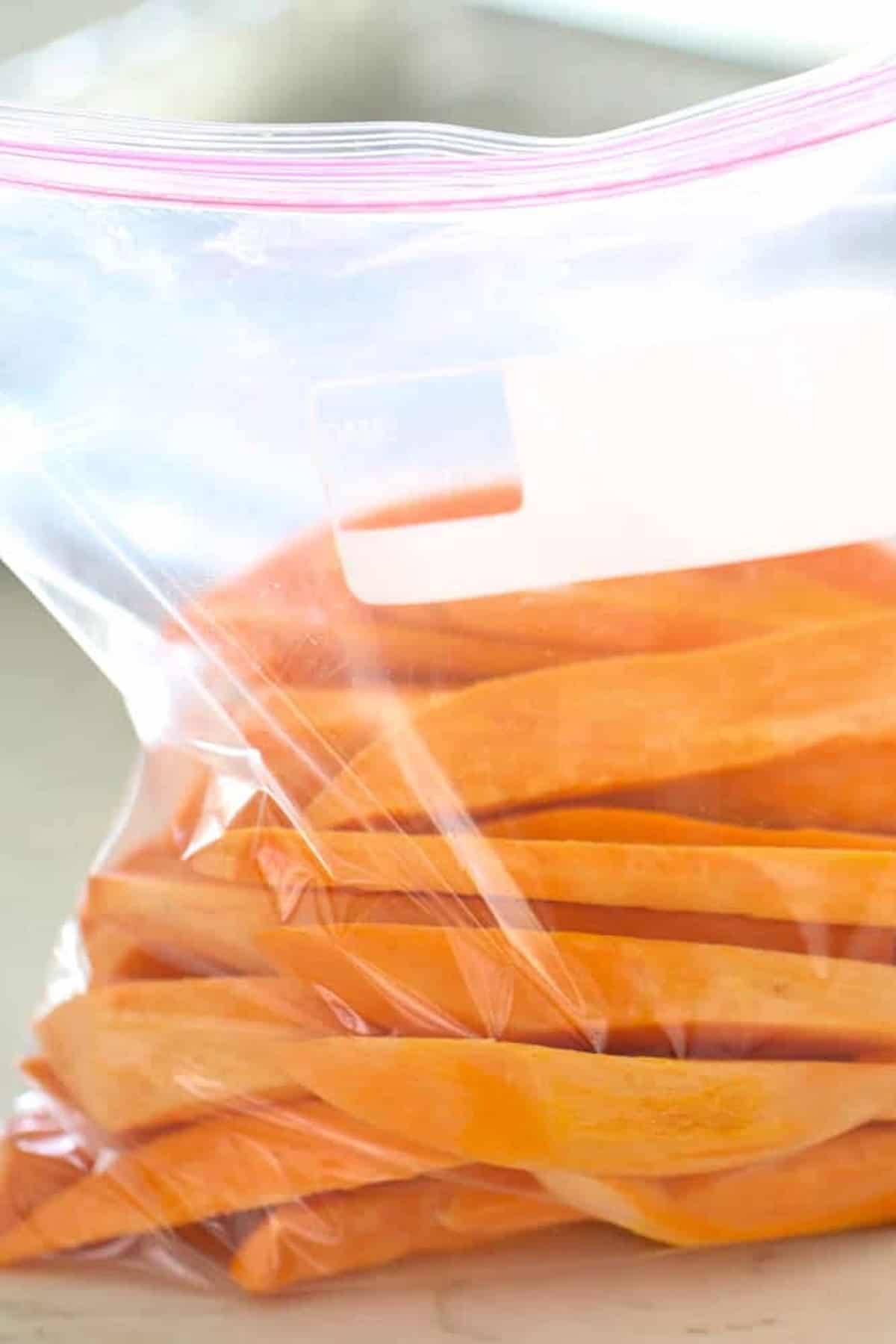 Sliced sweet potatoes in a transparent plastic zip-lock bag on a light surface.