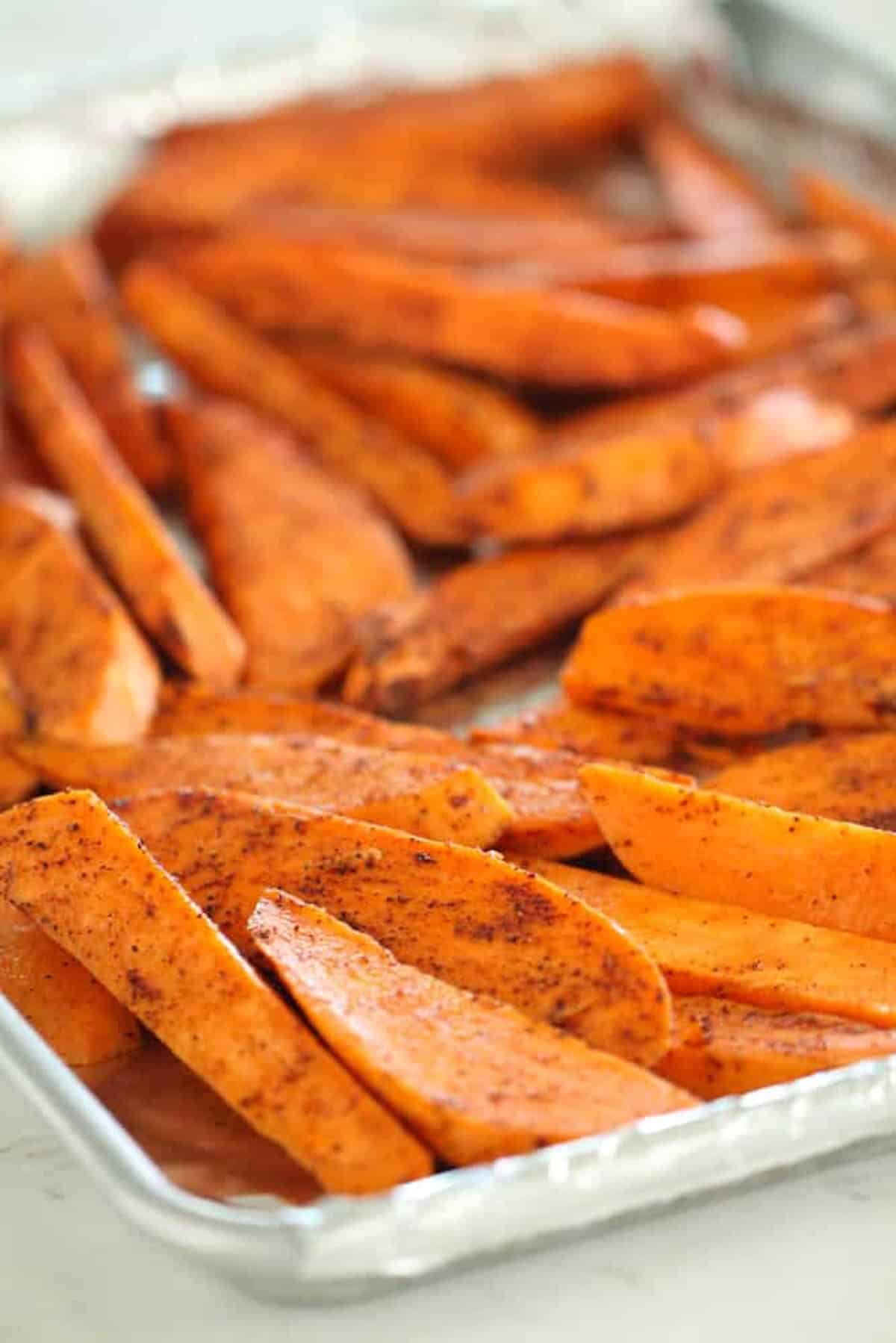 Seasoned sweet potato wedges arranged on a baking sheet.