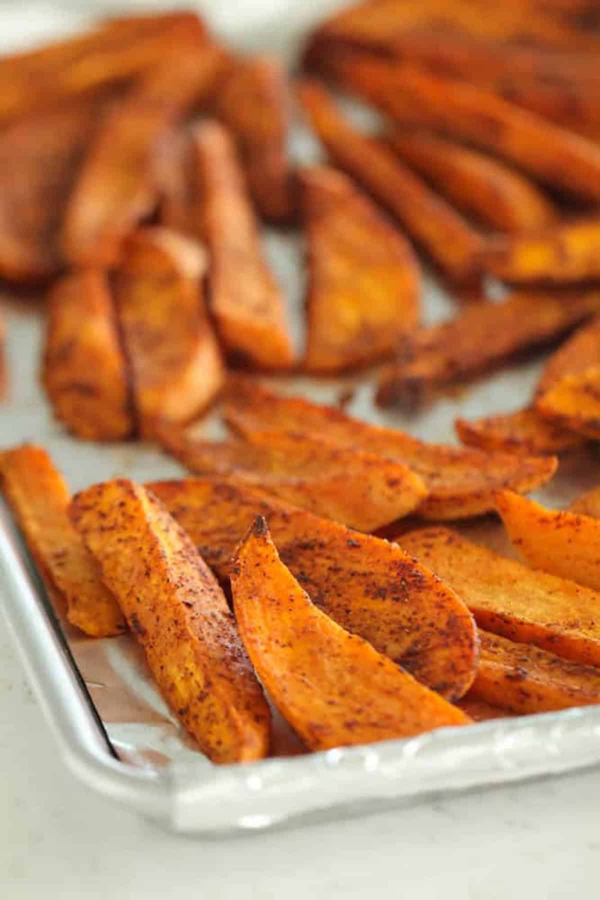 Sheet of seasoned, roasted sweet potato wedges on a baking tray.